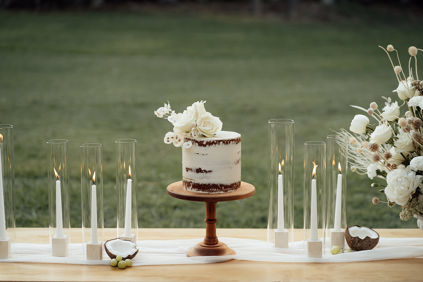 wedding cake on outdoor table with taper candles and glass cylinder sleeves